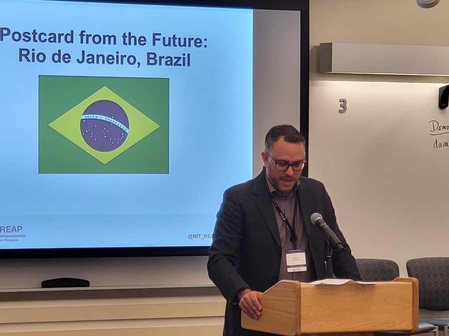 Homem ao pódio apresentando, com um slide sobre o Brasil ao fundo